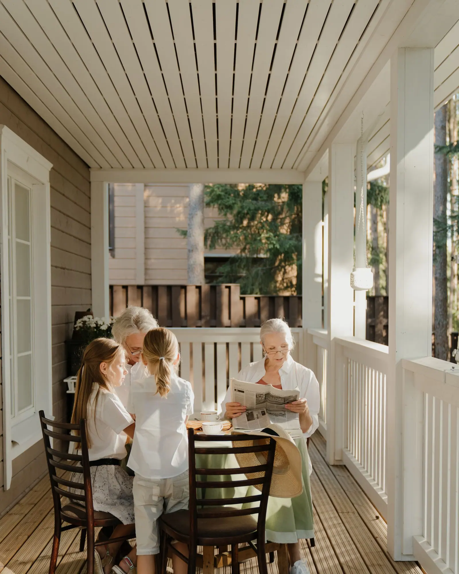 Three generations of a family sitting together at a table on a sunny veranda