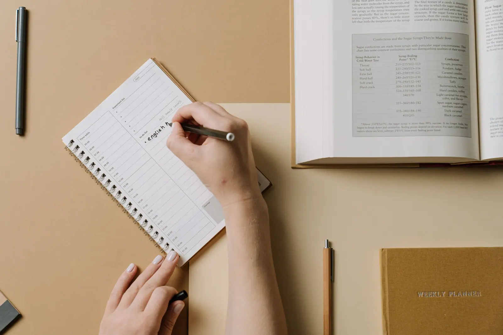 A hand writing in a planner beside a cup of coffee